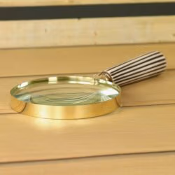 Handheld brass magnifying glass with a black and white striped handle, lying on a wooden desk.