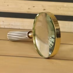 Close-up angled view of the decorative magnifying glass, highlighting the shiny brass rim and striped handle.