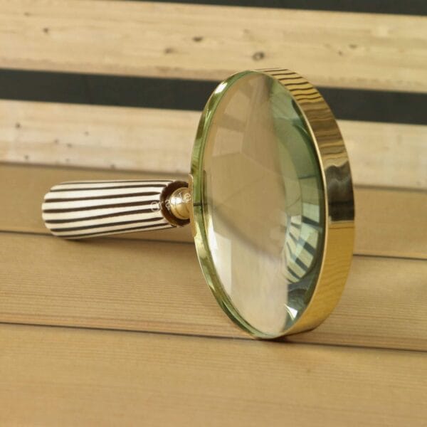 Close-up angled view of the decorative magnifying glass, highlighting the shiny brass rim and striped handle.
