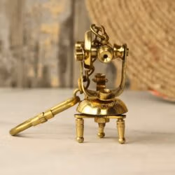 Front view of a miniature brass theodolite keychain designed as a vintage surveying instrument with a tripod base.
