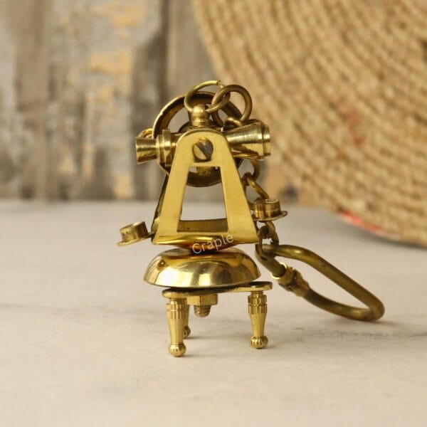 Back view of the collectible brass theodolite keychain, highlighting the tripod design and attached carabiner clip.