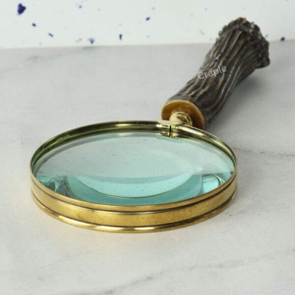 Detailed close-up of the 5X magnifying lens and the polished shiny brass frame of a handheld magnifier.