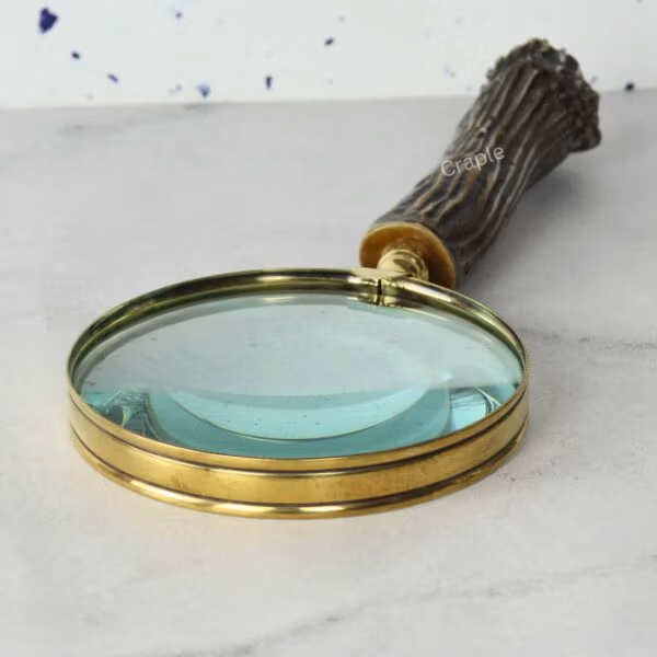 Detailed close-up of the 5X magnifying lens and the polished shiny brass frame of a handheld magnifier.