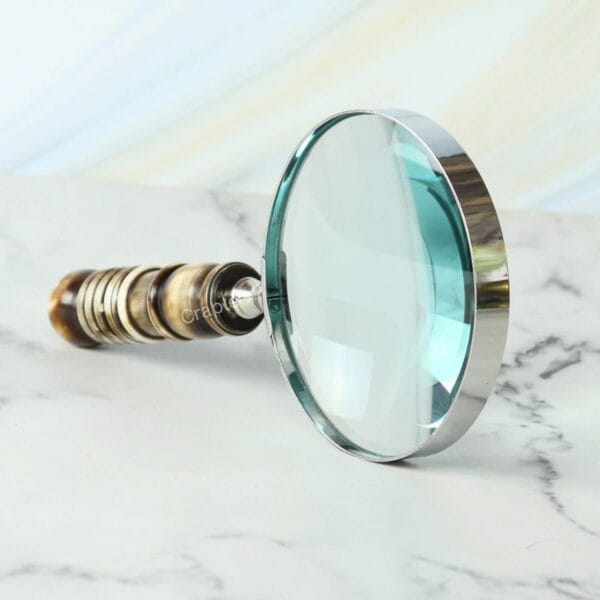 Handheld magnifying glass featuring a 5X lens, a polished nickel-finish frame, and a decorative turned resin handle.