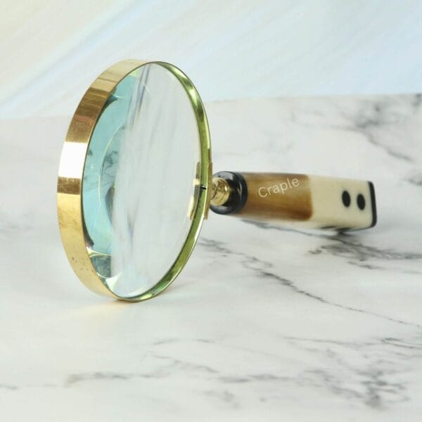 Close-up of the shiny brass frame and 5X lens on a magnifying glass with a distinctive domino-end handle.
