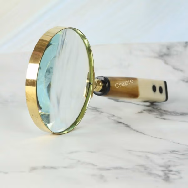 Close-up of the shiny brass frame and 5X lens on a magnifying glass with a distinctive domino-end handle.