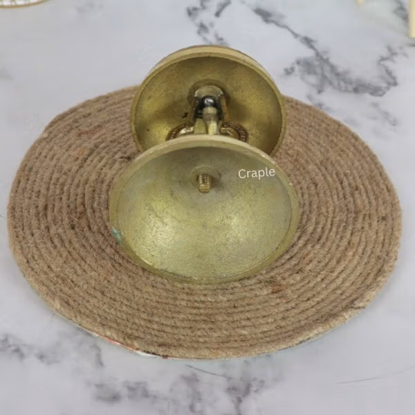 Top-down view of the ornate brass call bell, highlighting the detailed engraving on the bell and the push-button plunger.