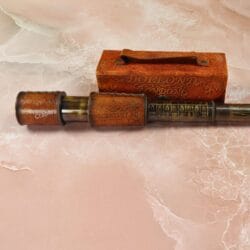 Vintage-style brass and leather telescope, partially extended, lying next to its embossed leather carrying case.