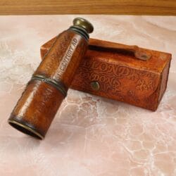 The leather-wrapped brass telescope in its compact, collapsed form, showing the intricate embossed leather.