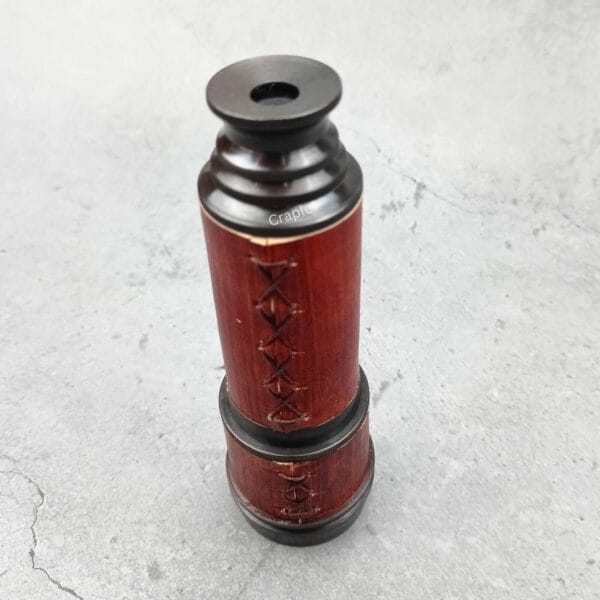 The antique brass and red leather telescope in its fully collapsed, compact form, standing upright.