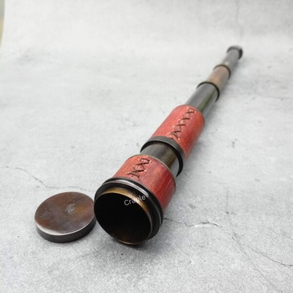 A brass and red leather nautical telescope partially extended, with its lens cap removed, ready for use.