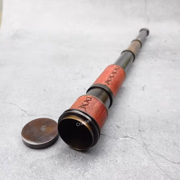 A brass and red leather nautical telescope partially extended, with its lens cap removed, ready for use.