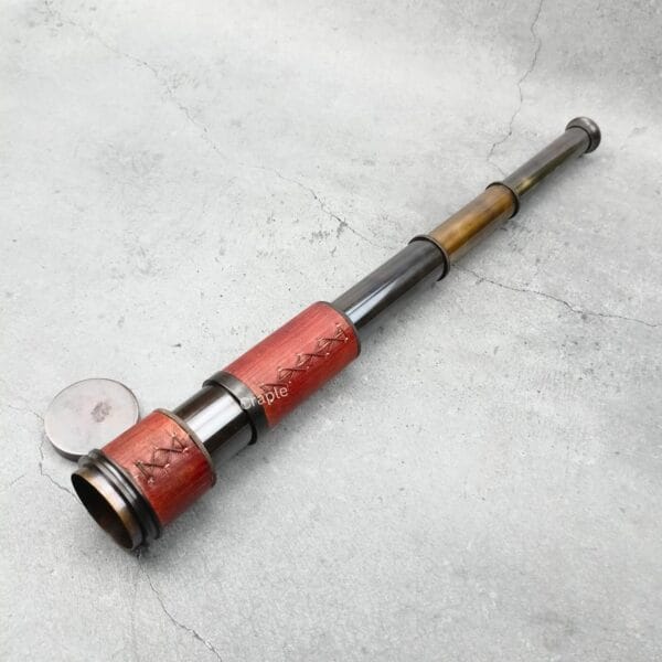 A full view of the extendable pirate-style brass telescope with its lens cap on the ground.