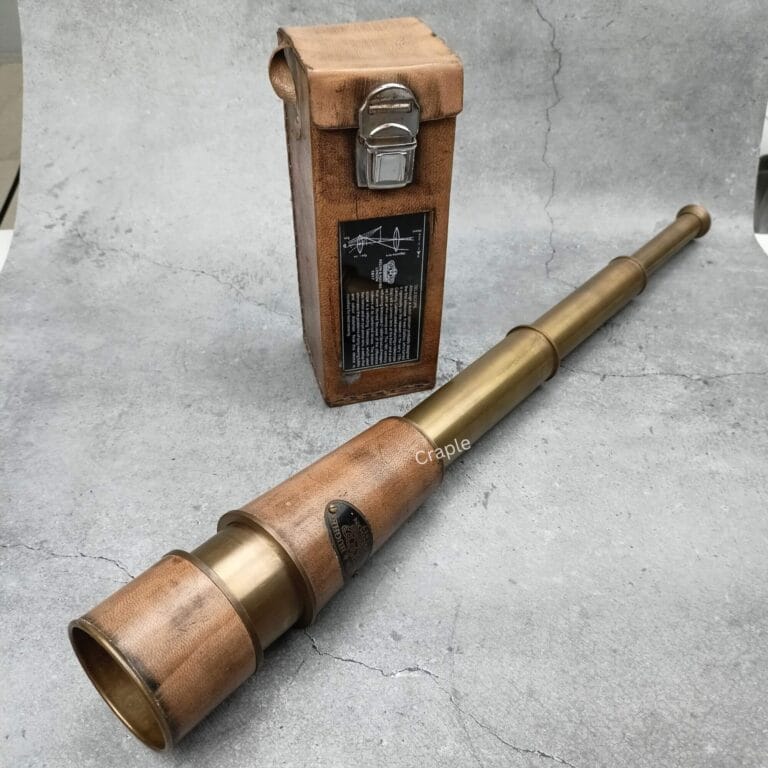 A fully extended Kelvin & Hughes antique brass telescope displayed next to its vintage brown leather carrying case.