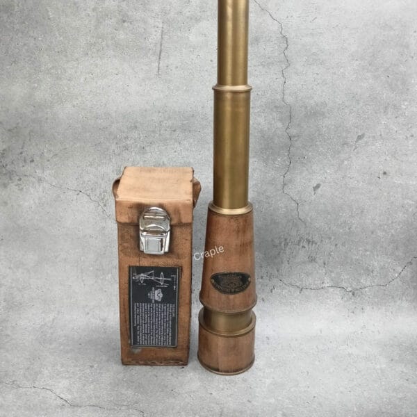 The tall, fully extended Kelvin & Hughes brass spyglass standing vertically next to its leather storage case.