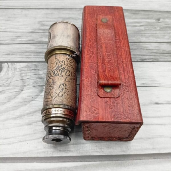 The compact brass and leather spyglass shown fully collapsed next to its protective, embossed red leather case.