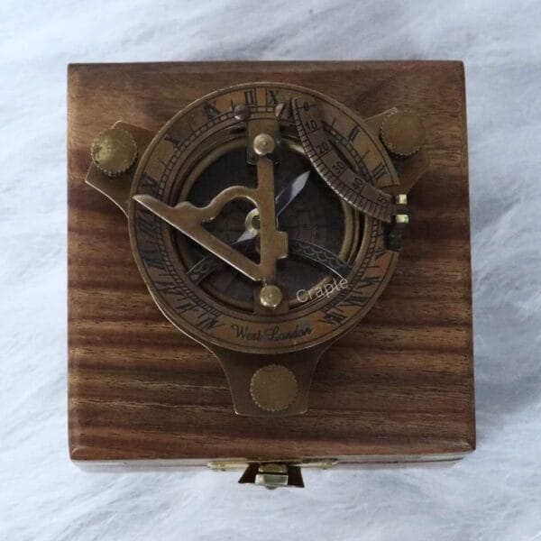 The brass sundial compass nestled inside its protective wooden display case with a velvet interior.