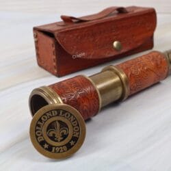 Close-up of the brass end cap on the spyglass, engraved with "Dollond London 1920", next to its embossed leather case.