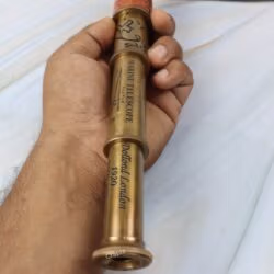 A hand holding the extended brass marine telescope, showing the engraved "Dollond London" text along the barrel.