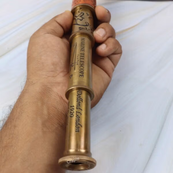 A hand holding the extended brass marine telescope, showing the engraved "Dollond London" text along the barrel.