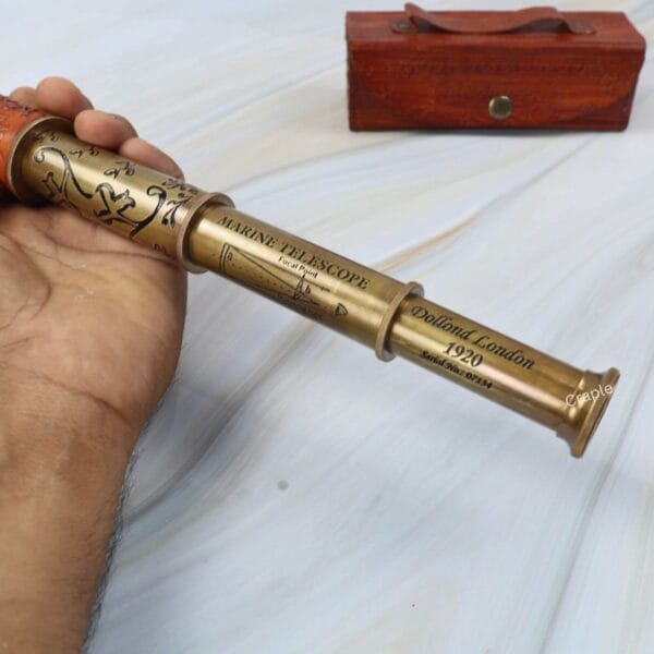 A hand extending the collapsible brass spyglass to its full length, revealing the multiple barrels.