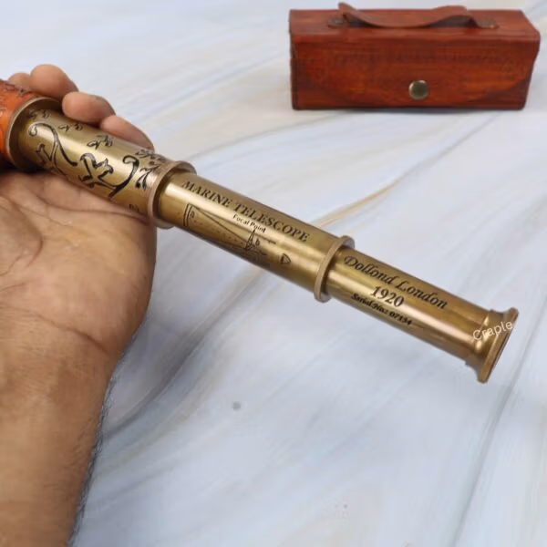 A hand extending the collapsible brass spyglass to its full length, revealing the multiple barrels.
