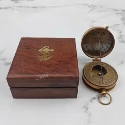 Antique brass pocket sundial compass shown open next to its closed wooden box which features a brass anchor inlay.