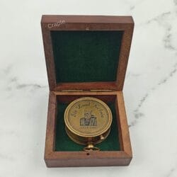 The back of the antique brass pocket compass, engraved with 'Made for Royal Navy, London', resting in its wooden box.