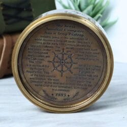 The engraved bottom of the antique brass compass, featuring historical text and a nautical ship's wheel design.