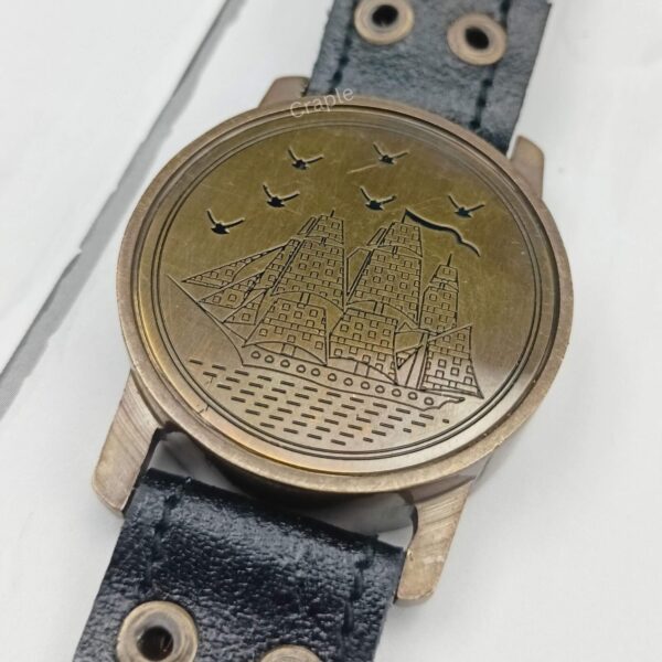 Detailed close-up of the embossed sailing ship and birds on the brass lid of the wrist compass.
