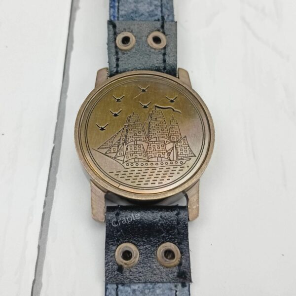 The back of the brass wrist compass showing the protective lid with an embossed nautical sailing ship design.