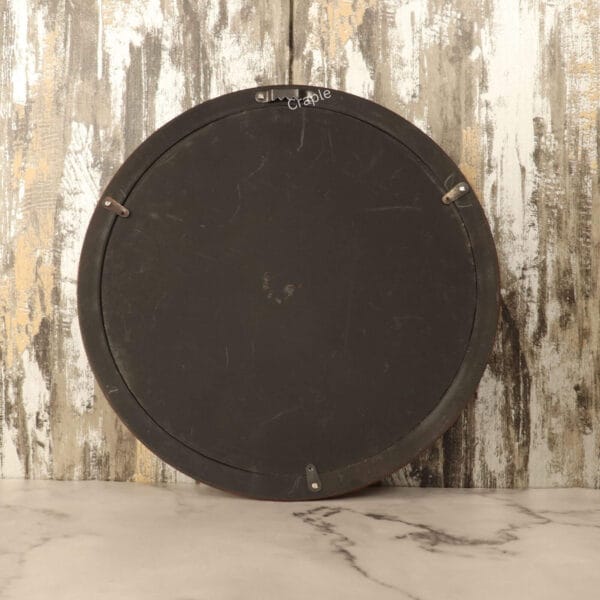 The back of the round wooden wall clock, showing the battery mechanism and the built-in metal hanger for easy installation.