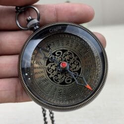 Close-up of an antique brass pocket compass with a black finish, held in hand to show the intricate vintage dial.