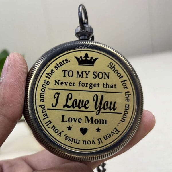 A hand holding the antique brass compass to display the sentimental "Love Mom" engraving for a son.