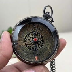 A clear view of the entire antique compass dial with its black casing and red-tipped needle, held in hand.