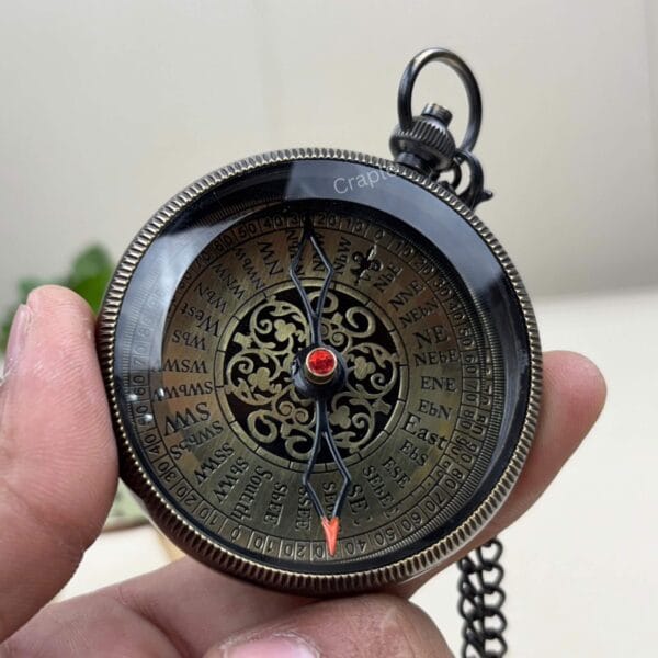 A clear view of the entire antique compass dial with its black casing and red-tipped needle, held in hand.