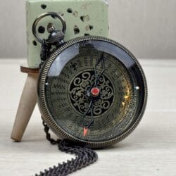 The black antique pocket compass resting on a surface with its matching black chain.