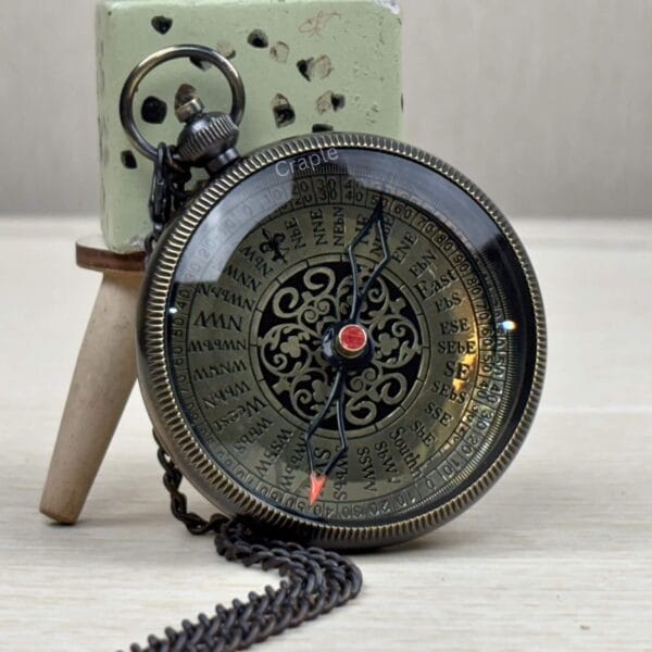 The black antique pocket compass resting on a surface with its matching black chain.