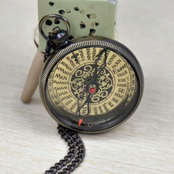 The vintage brass and black pocket compass with chain, displayed at an angle.