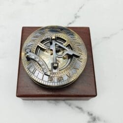 Black antique brass sundial compass with its lid closed, resting on a polished square wooden display box.