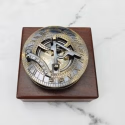 Black antique brass sundial compass with its lid closed, resting on a polished square wooden display box.