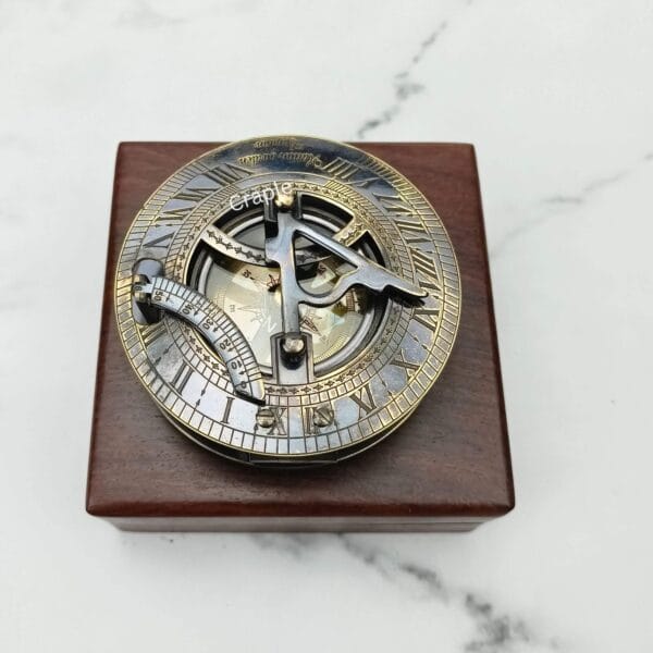 Black antique brass sundial compass with its lid closed, resting on a polished square wooden display box.