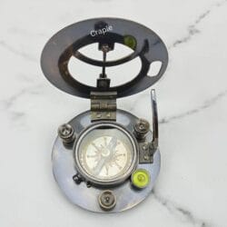 Angled view of the open black brass sundial compass, showing the hinge mechanism and internal details.