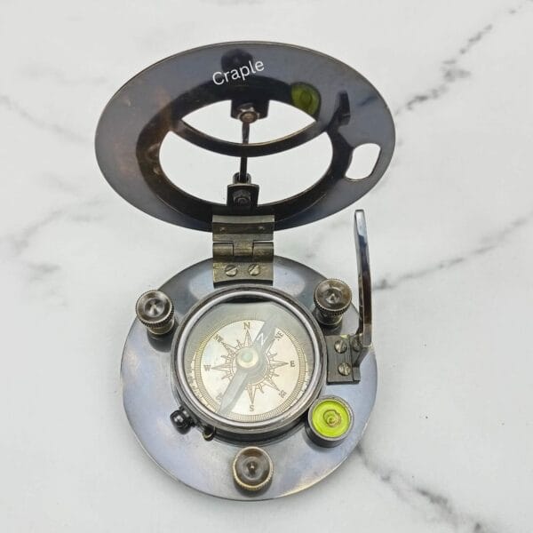 Angled view of the open black brass sundial compass, showing the hinge mechanism and internal details.