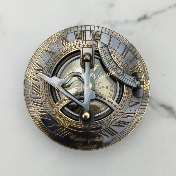 Top-down view of the black antique sundial compass face, detailing the gnomon, latitude arc, and Roman numerals.