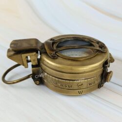 Angled side view of a closed antique brass British WWII prismatic compass, showing the side markings and hinge.