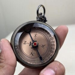 Antique black brass pocket compass with a detailed dial and cardinal points, held in a person's hand.