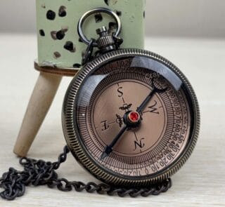 Engraved brass pocket compass for a son, featuring a black antique finish and a matching chain on a wooden surface.