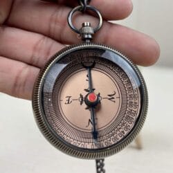 Detailed view of the antique-style face of the brass pocket compass, showing the needle and degree markings.