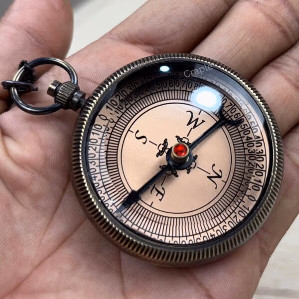 Angled view of the black antique brass compass held in hand, showing the glass cover and textured edge.